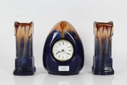 Art Deco style pottery three piece clock garniture, with oval timepiece and navy blue and brown