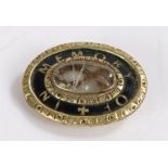 Late Victorian mourning brooch on a gilded metal base with "In memory of" monogrammed onto a black