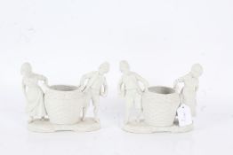 Pair of bisque figural vases, each in the form of a boy and girl moving a large wicker basket,