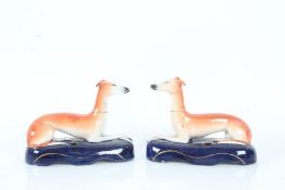 Pair of Staffordshire Greyhounds in a reclined position on blue bases, 17cm long