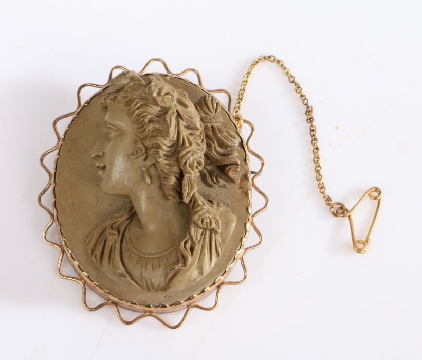 A cameo brooch made from carved lava, set a yellow metal with a safety chain. Weighing 26 grams.