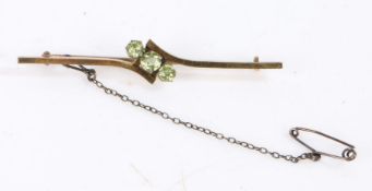 A 9ct gold bar brooch set with three peridots and a safety chain. Approx. length 55mm. Weighing 3.