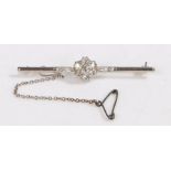 A platinum bar brooch with a flower shaped diamond cluster and safety chain. Approx. total diamond