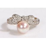 A white metal diamond bow shaped ring with one pinkish pearl. Approx. total diamond carat weight: