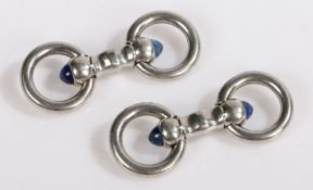 A pair of platinum Cartier stirrup cuff-links with a blue sapphire cabochon at each end. Stamped