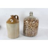 Large stoneware flagon together with a large glass bottle full of wine corks (2)