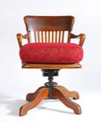 An early 20th Century oak swivel desk chair, the curved back above slats and a cushion flanked by