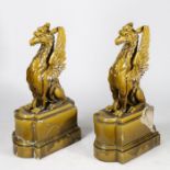 Pair of pottery griffins, in an olive green glaze seated on a stepped plinth base, both AF, 96cm