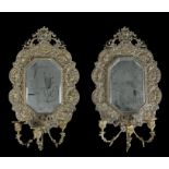 Pair of brass wall mirrors, the shaped and bevelled mirror plate within a decorative frame featuring