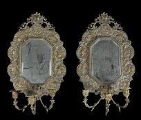 Pair of brass wall mirrors, the shaped and bevelled mirror plate within a decorative frame featuring