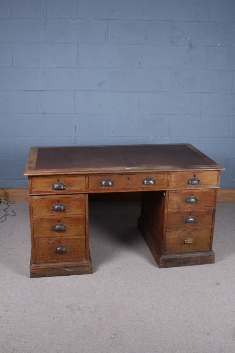 A 20th century oak twin pedestal desk with a brown leather inset top above nine drawers raised on