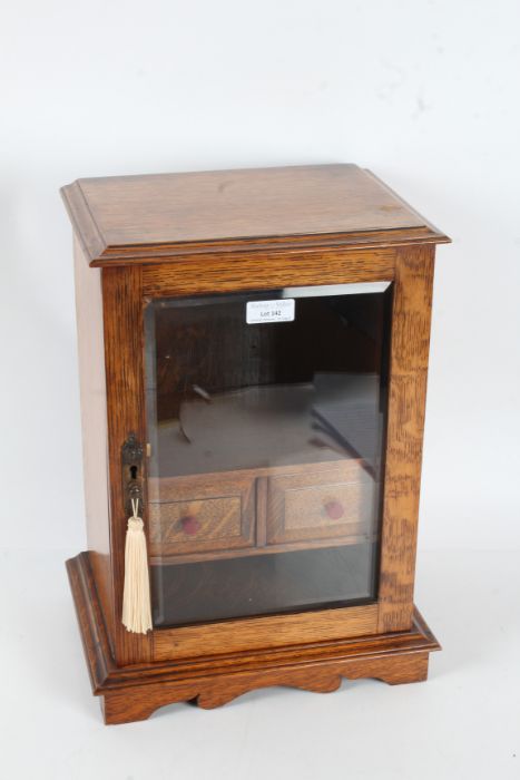 Golden oak smokers cabinet, having a single glazed door enclosing an interior with two drawers, 39.