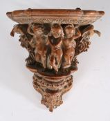 18th Century walnut wall bracket, the shaped shelf above carved depictions of dancing putti