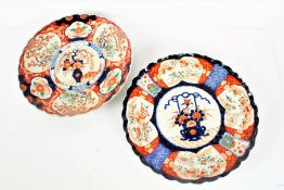 Two Japanese Imari plates, each centred with vases of flowers in navy, iron red, and gold on a white