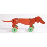 An early 20th Century Folk Art articulated wooden pull-along toy dog, painted in red with green
