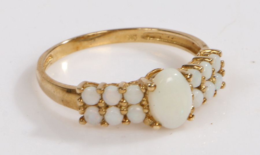 A 9 carat gold and white opal ring, the head set with thirteen claw set opals, with one central oval
