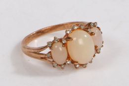 A 9 carat gold ring, the head set with three claw set opaque white stones surrounded by diamonds ,