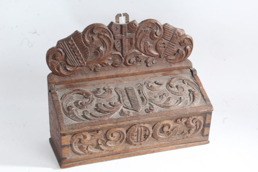 A 19th century carved oak candle box, carved in relief with a shield shape crests, with a carved