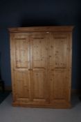 20th century pine three door wardrobe, the tapering pediment above three panelled doors opening to