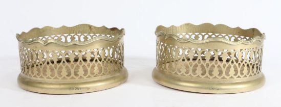 A pair of silvered-brass bottle coasters Of leafy S-scroll open-work, with reeded wavy rim and