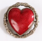A red enamel brooch in the form of a heart, the border depicting clasped hands, set on unmarked