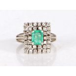 An 18 carat white gold emerald and diamond ring, having an emerald to the centre, set on a raised