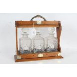 Edwardian electro plate mounted oak tantalus, containing three clear glass decanters with