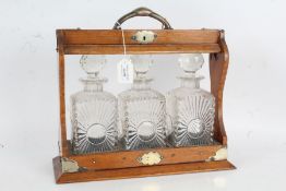 Edwardian electro plate mounted oak tantalus, containing three clear glass decanters with