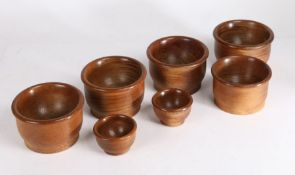 Seven turned wooden coin pots, the largest 13.5cm diameter, 8.5cm high, the smallest 8m diameter,