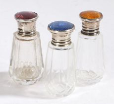 Three George V silver and clear glass perfume bottles, the lids with orange, lilac and dark blue
