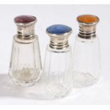 Three George V silver and clear glass perfume bottles, the lids with orange, lilac and dark blue