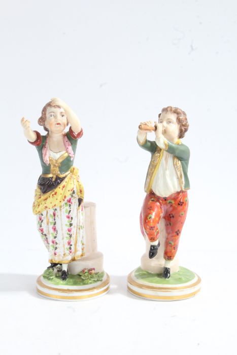 A pair of 19th century figures, baring Derby Marks, one depicting a young boy playing a pipe the