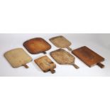 Six rustic chopping boards, the majority with tapering handles above rectangular and shaped