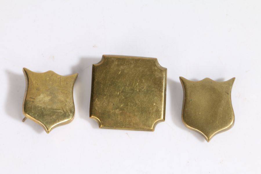 Brass escutcheons from a wooden trunk, two shield shaped, the third a square with notched corners,