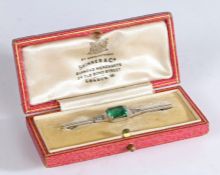 A white metal late Art Deco bar brooch, featuring an emerald cut green stone to the centre, with