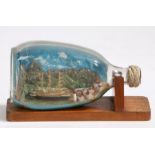 Ship in a bottle, depicting a three masted ship moored in a harbour with volcano and hills to the