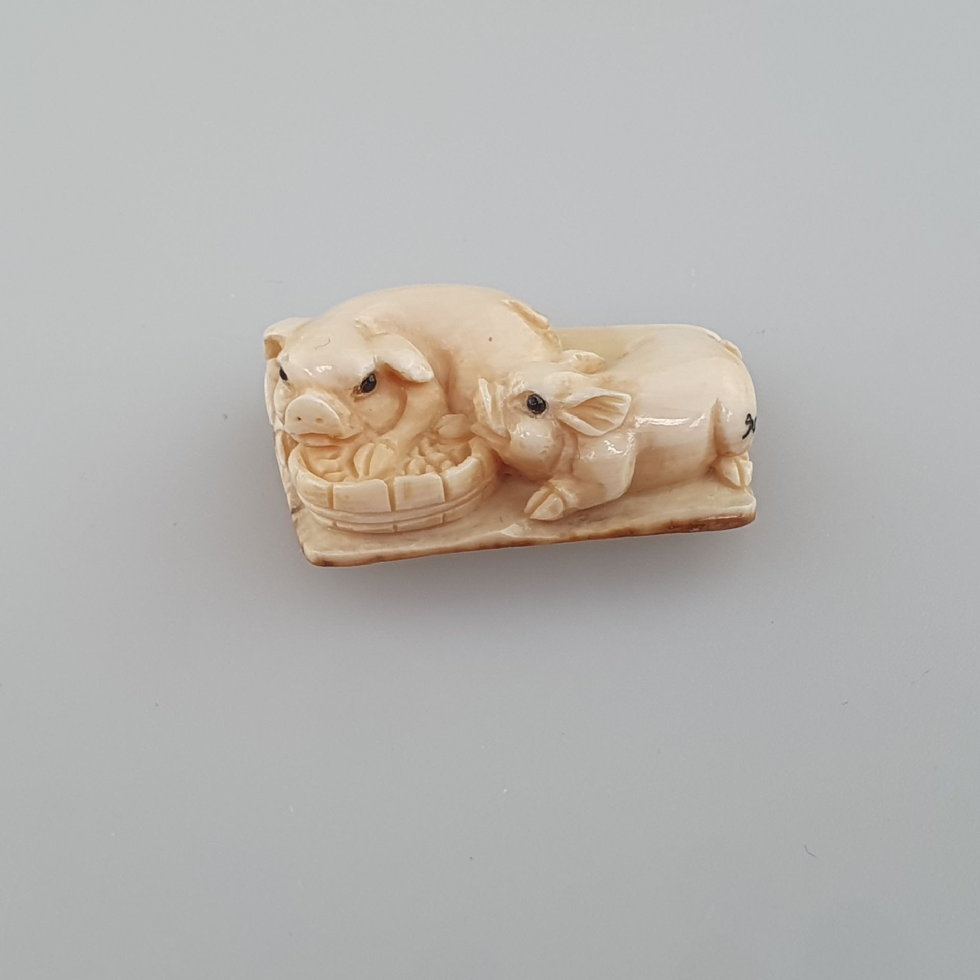 Netsuke - Zwei Schweinchen am Trog, Mammutbein, geschnitzt, dunkel eingelegte Augen, signiert,