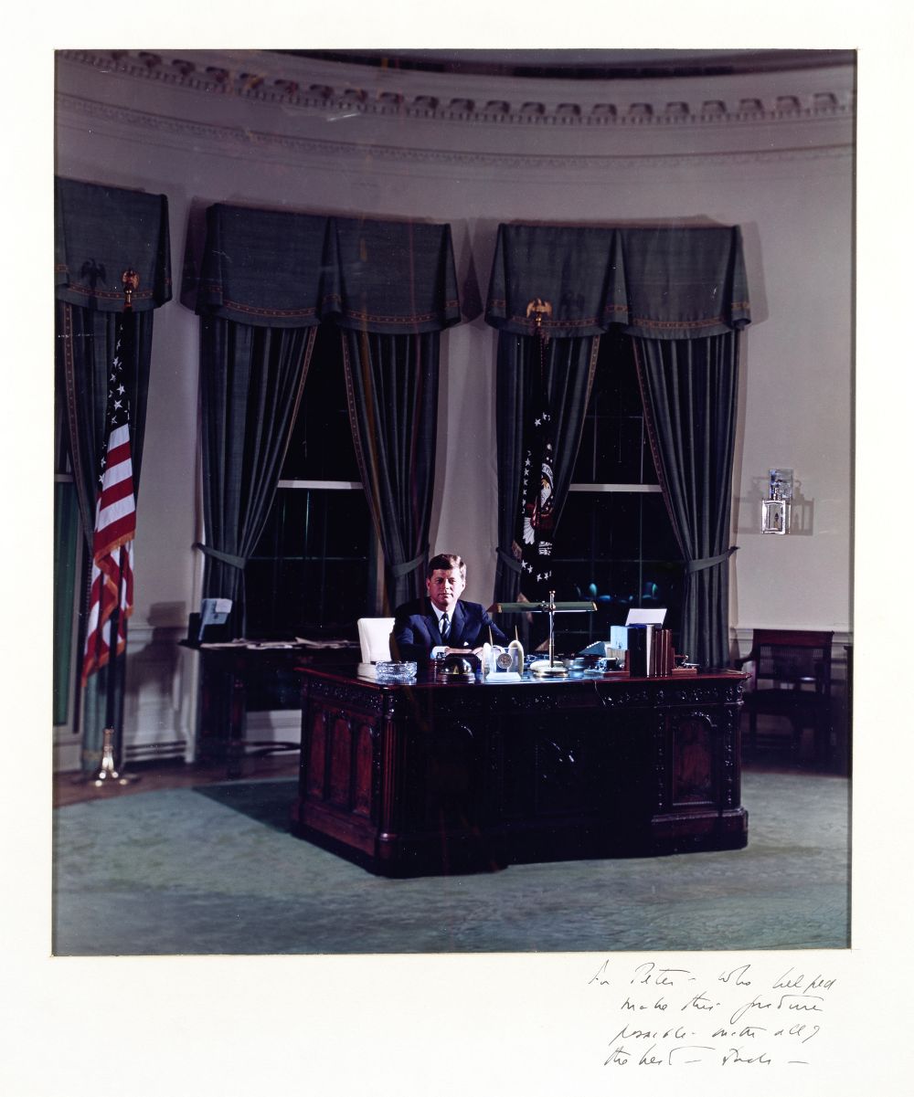 KENNEDY (JOHN F.) Colour portrait photograph depicting John F. Kennedy sitting behind the Resolut...