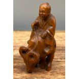 A Japanese hand carved netsuke of a elderly gentleman riding an ox. [5cm in length]