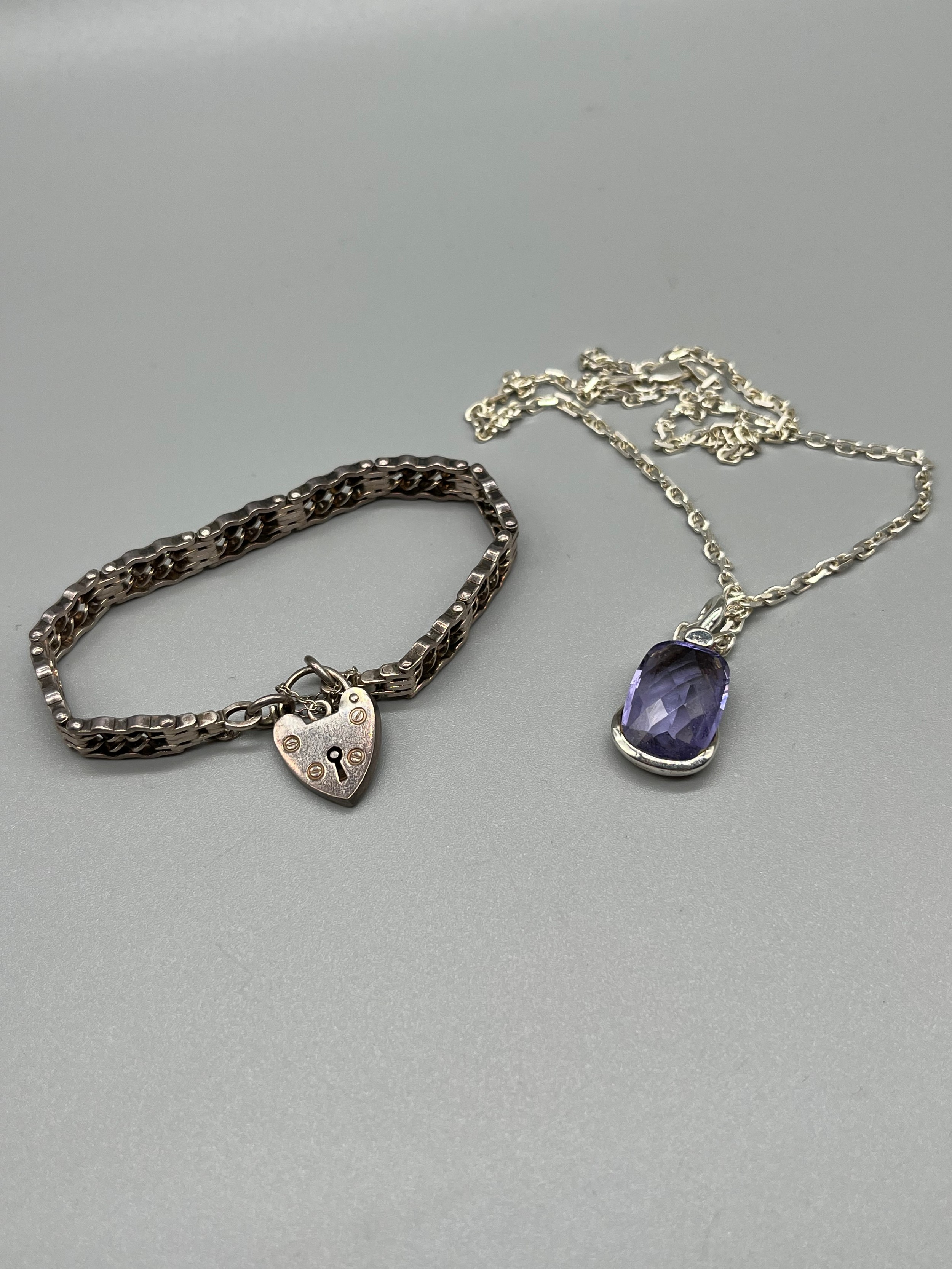 A Silver bracelet with heart lock attached, together with a silver and purple stone pendant with