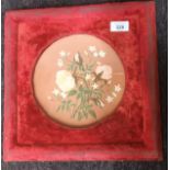 A Red velvet frame containing a hand painted Watcombe Torquay ware plate depicting a floral design.