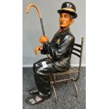 A Large Charlie Chaplin seated figure, comes with a metal chair. [57cm high]