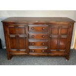 Ercol dark elm wood sideboard, the shaped rectangular surface above a bank of four drawers,