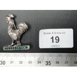 A silver cockerel figure on emerald platform