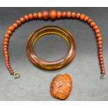 Three items of amber, Includes graduated bead necklace, carved ingot/ pendant and bangle.