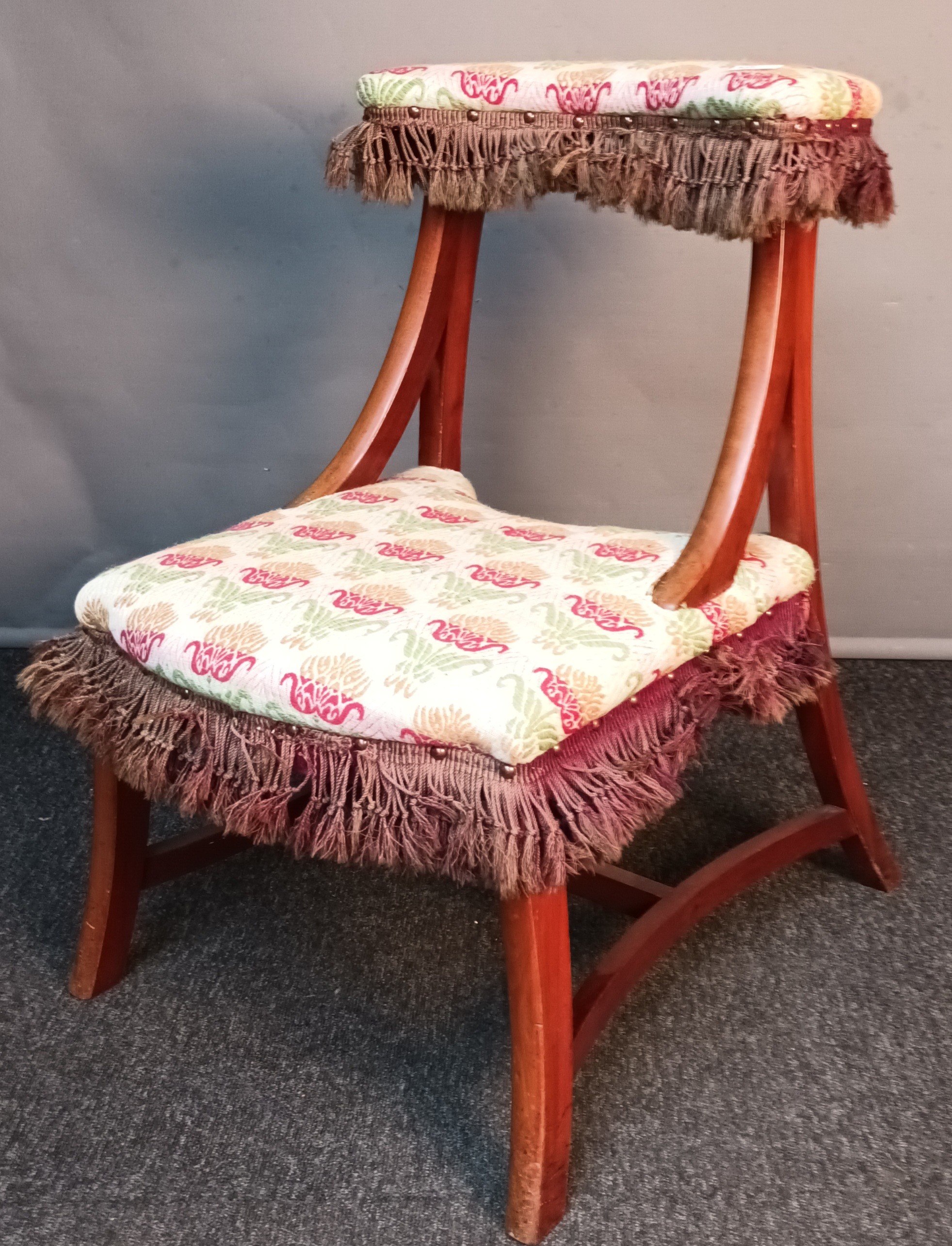 19th century prayer stool/ chair, upholstered in a floral material with brown fringe, raised on
