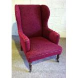 A late Victorian wing armchair, currently upholstered in claret, with turned front legs and castors