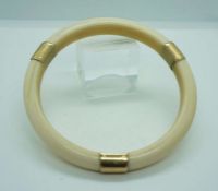 An 18 carat gold mounted ivory bangle, early 20th century, the plain hoop with three gold