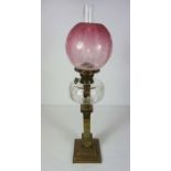 A Victorian brass column oil lamp, circa 1870, with a cranberry glass shade, clear reservoir and the