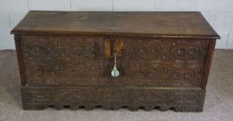 A 17th century oak coffer, with a profusely carved front, the hinged and moulded rectangular top